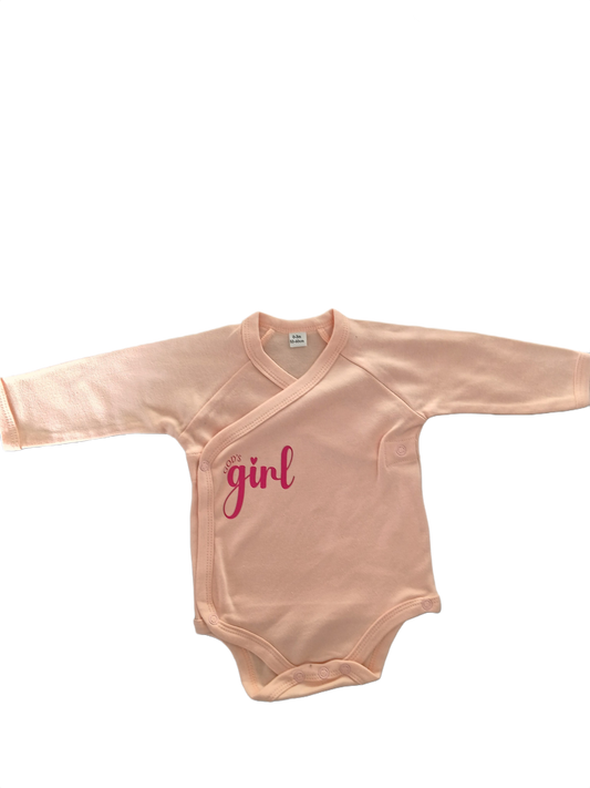 A long-sleeve baby bodysuit in a soft peach-pink color, featuring a light pink 'God's Girl' text graphic on the chest.